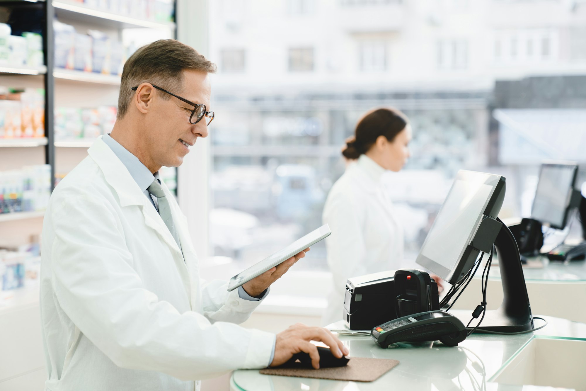 Druggists working together at cash point desk in drugstore pharmacy using computer and tablet